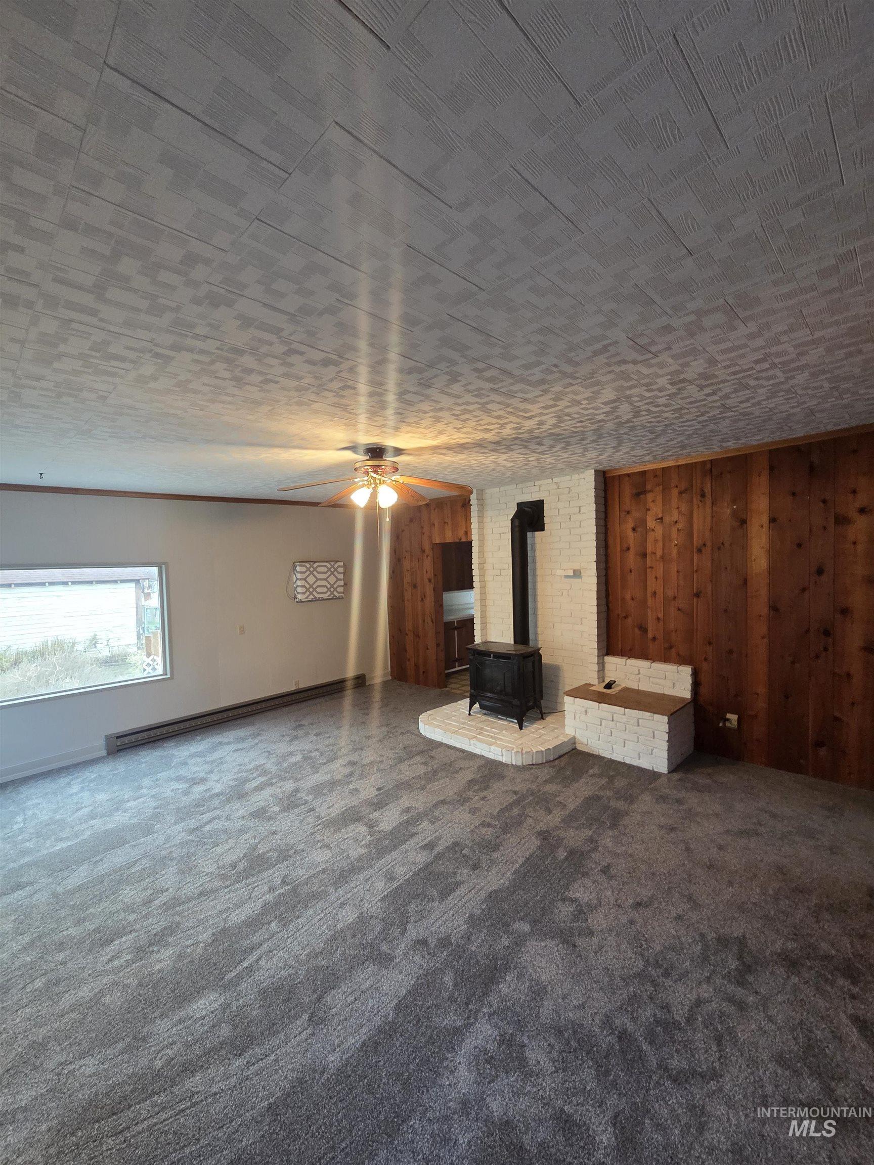 465 South 15th Street Pomeroy, WA 99347 - Photo 12 of 24 Unfurnished living room featuring a wood stove, a ceiling fan, dark carpet, a baseboard radiator, and wooden walls