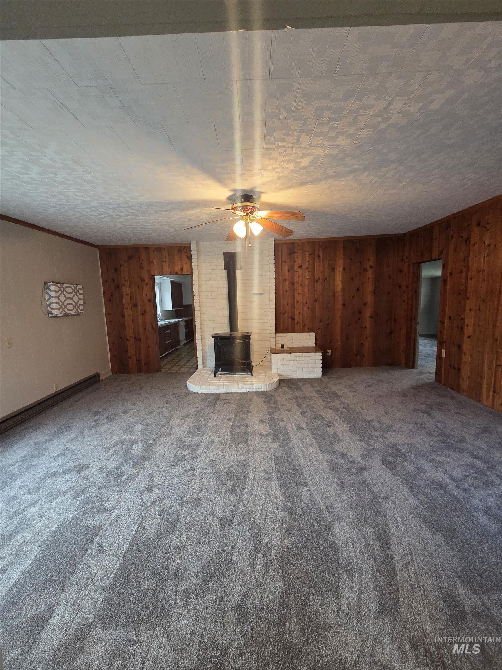 465 South 15th Street Pomeroy, WA 99347 - Photo 13 of 24 Unfurnished living room with wooden walls, a wood stove, ceiling fan, and carpet floors