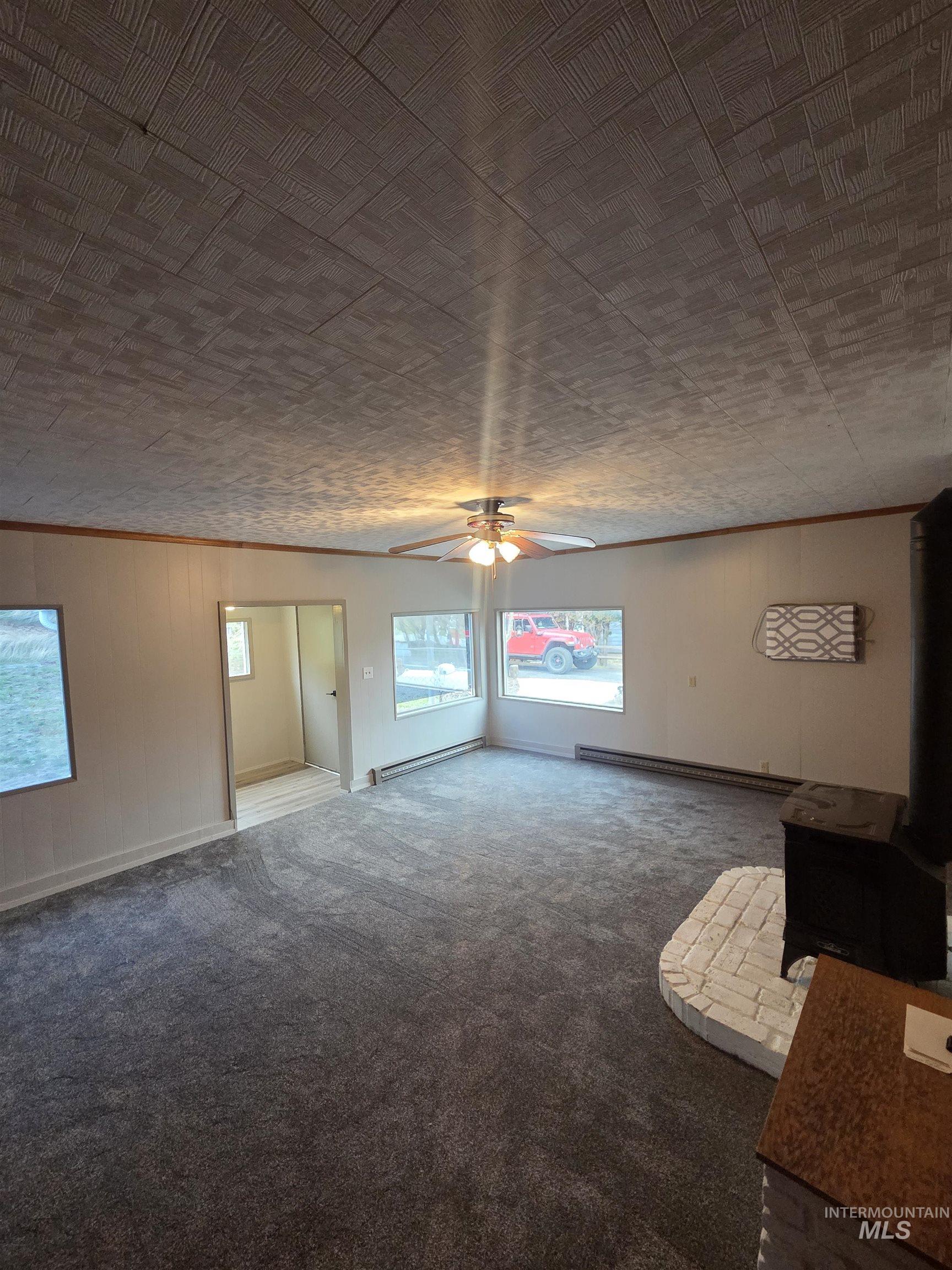 465 South 15th Street Pomeroy, WA 99347 - Photo 14 of 24 Unfurnished living room featuring a wood stove, wooden walls, crown molding, a baseboard heating unit, and a ceiling fan