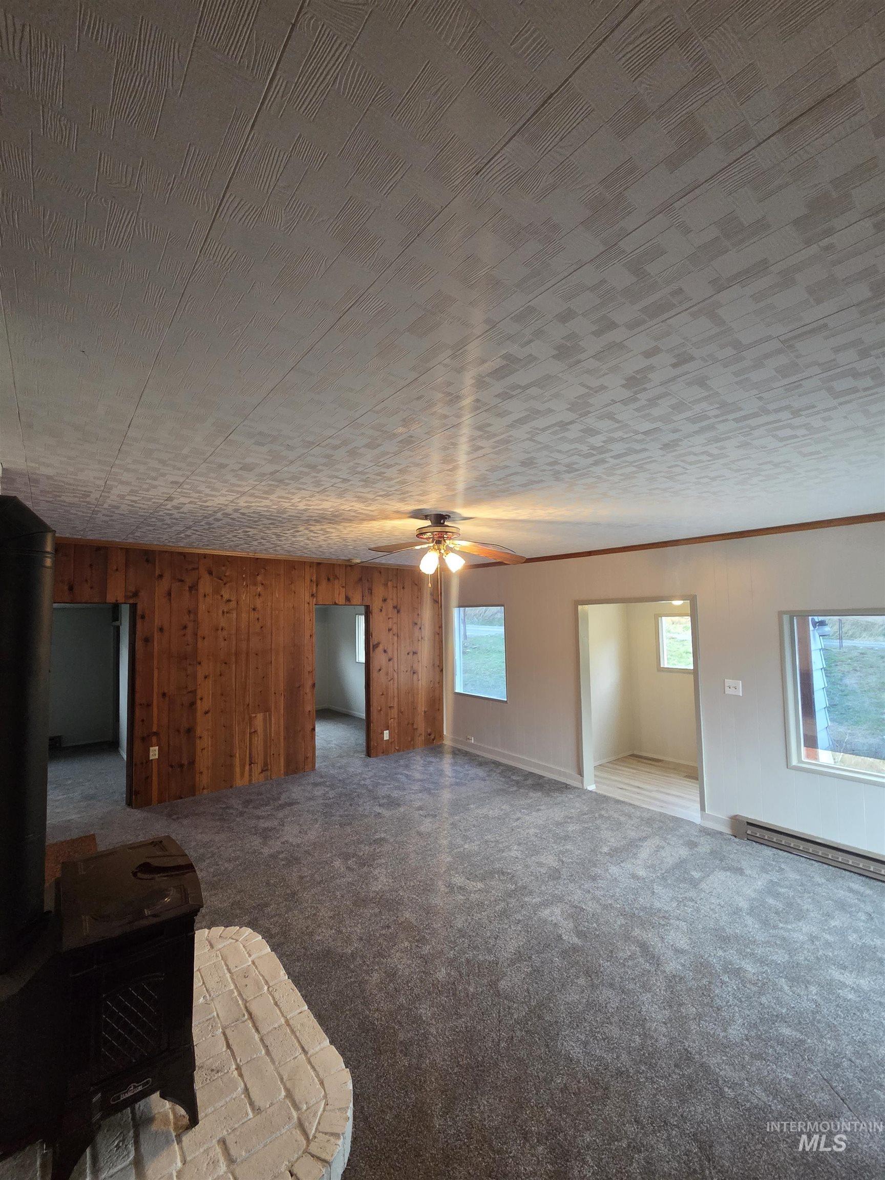 465 South 15th Street Pomeroy, WA 99347 - Photo 15 of 24 Unfurnished living room featuring wooden walls, a wood stove, carpet, a baseboard heating unit, and ceiling fan