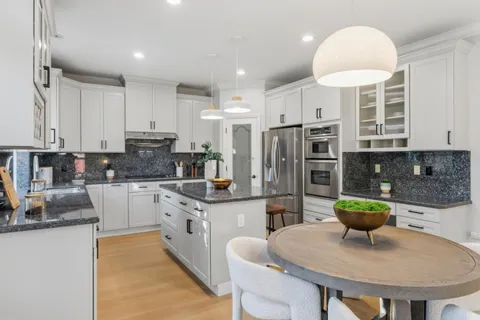 a kitchen with stainless steel appliances kitchen island granite countertop a table chairs and a refrigerator