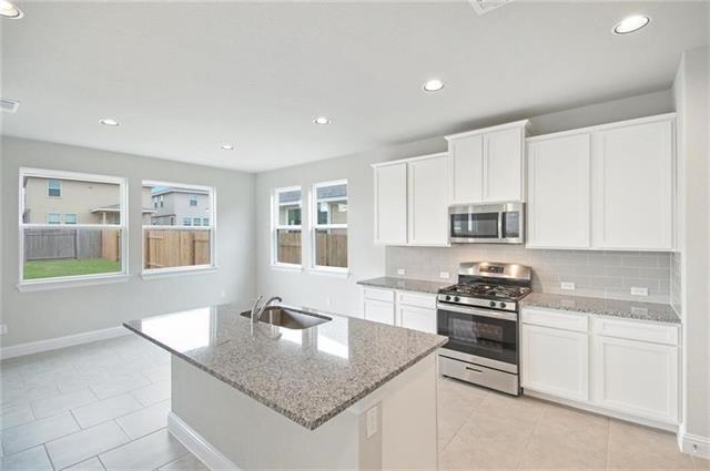 113 Gaida Loop Georgetown, TX 78628 - Photo 9 of 23 Kitchen featuring light stone countertops, appliances with stainless steel finishes, white cabinetry, backsplash, and light tile patterned floors
