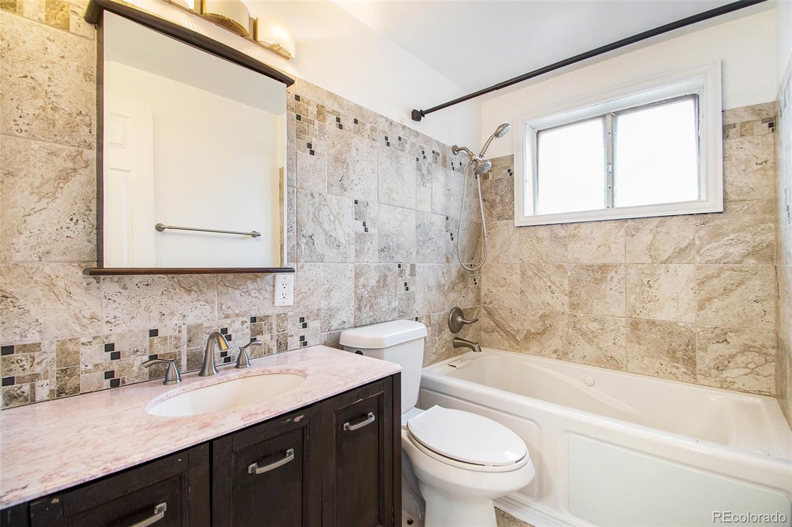 8360 Emerson Street Denver, CO 80229 - Photo 10 of 13 a bathroom with a granite countertop sink a toilet a mirror a bathtub and shower