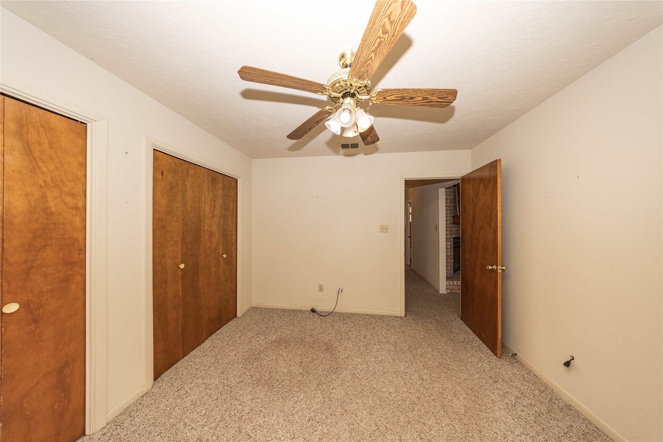 2501 Fischer Store Road Wimberley, TX 78676 - Photo 9 of 23 Carpeted room featuring a ceiling fan with integrated lighting, two wood-paneled closet doors, and an additional wood-paneled door
