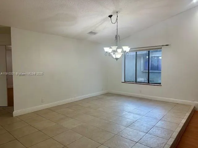 an empty room with chandelier fan and kitchen view