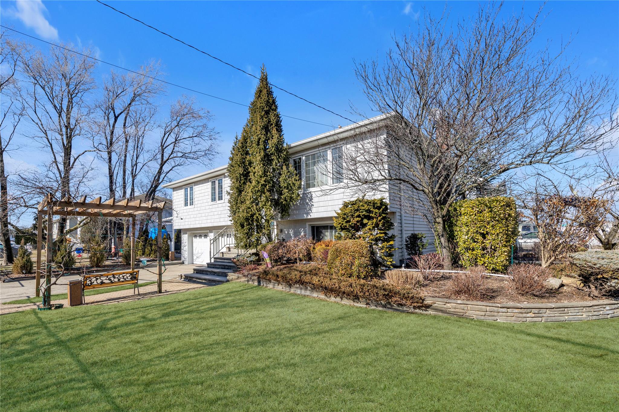 View of front of home with an attached garage, driveway, a front lawn, and a pergola