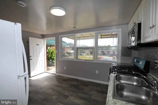 a kitchen with granite countertop a refrigerator a sink a stove a window and cabinetry