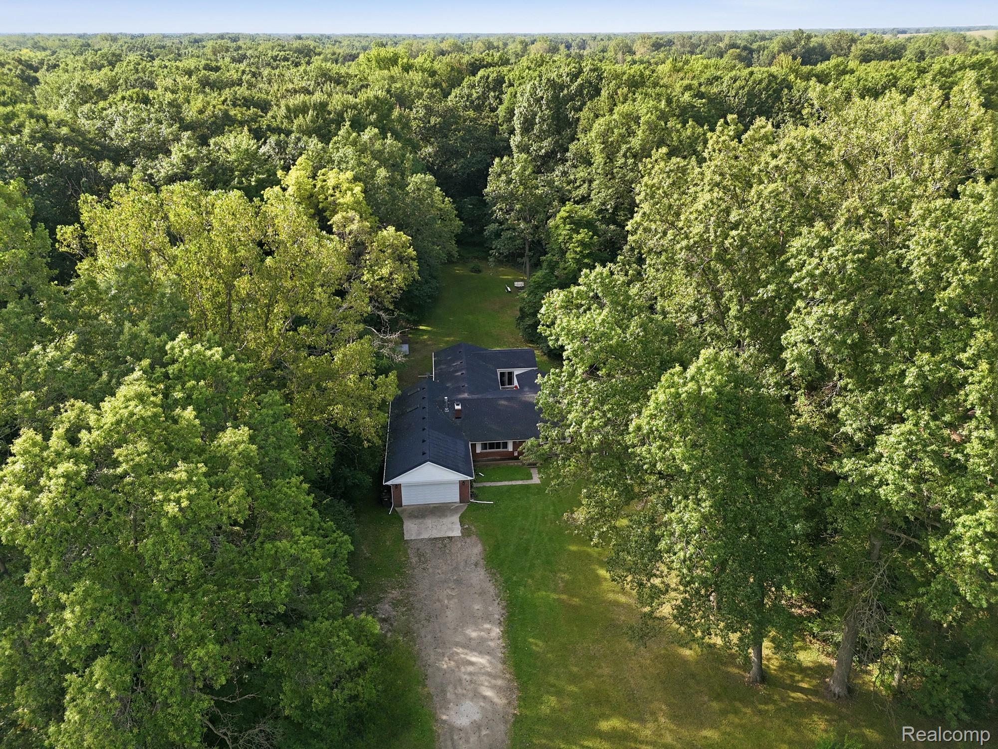 45223 Wear Road Belleville, MI 48111 - Photo 5 of 60 Expansive property featuring a black asphalt shingle roof, attached garage, and a long gravel driveway, all surrounded by mature deciduous trees