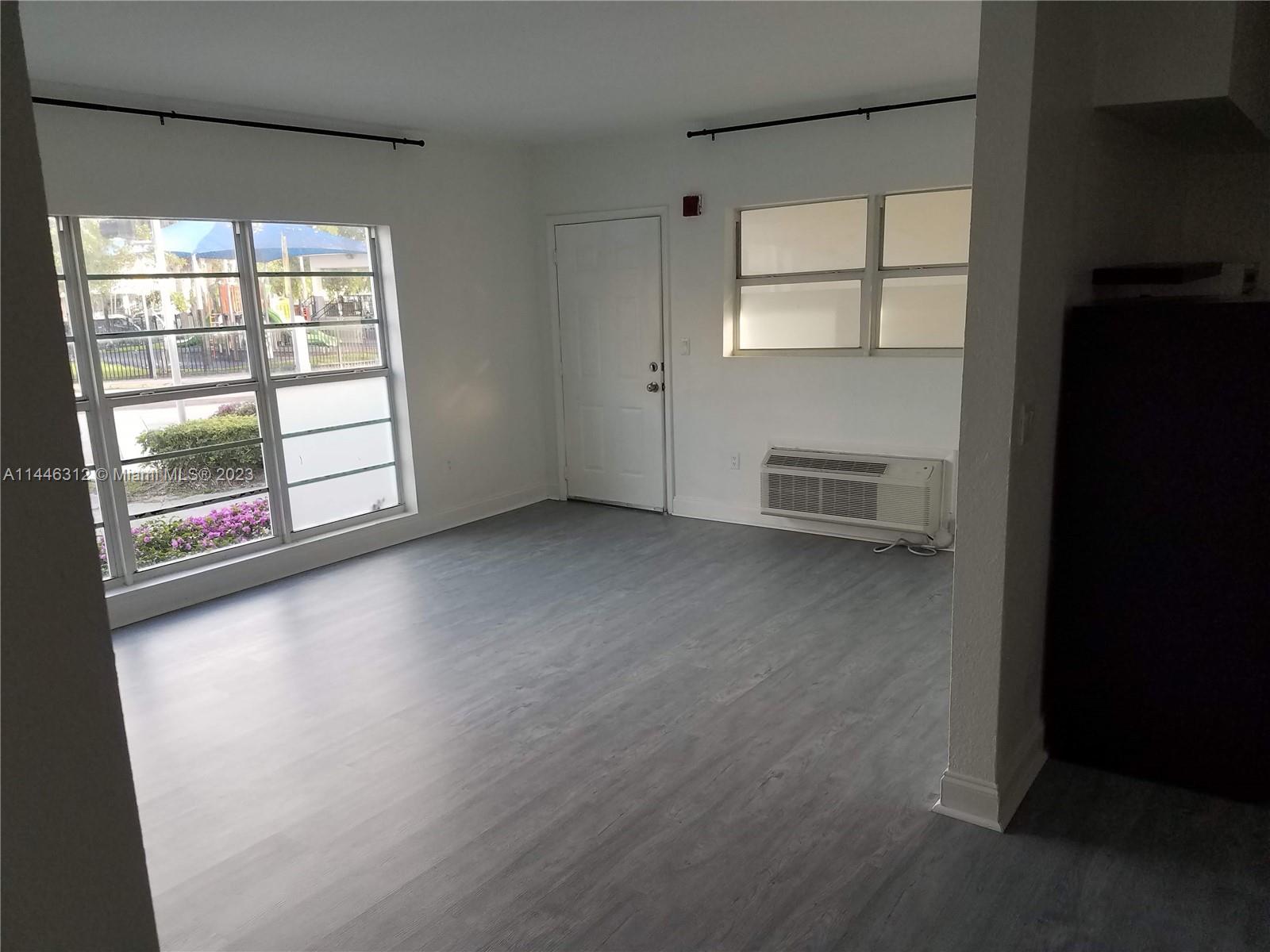 an empty room with windows and view of kitchen
