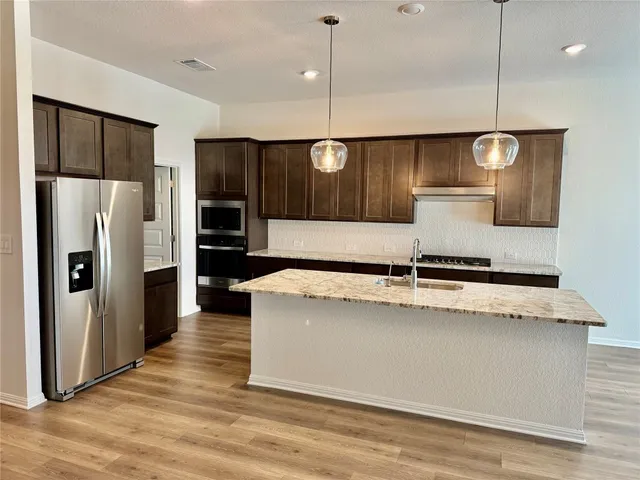 a kitchen with kitchen island a counter top space a sink a refrigerator and chairs