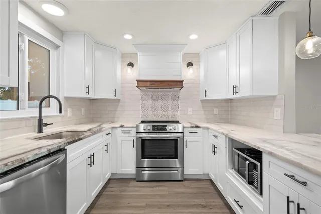 a kitchen with stainless steel appliances granite countertop a sink a stove a refrigerator and a wooden floor