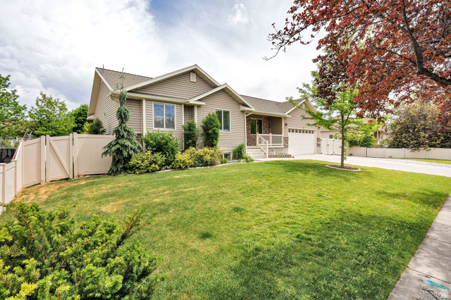 Siding exterior with a two-car garage, manicured lawn, established landscaping, and a privacy fence