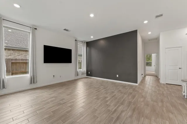a view of an empty room with wooden floor and a flat screen tv