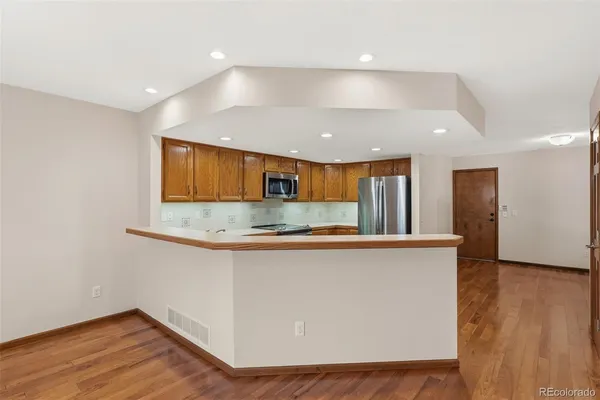 a kitchen with stainless steel appliances granite countertop a sink a microwave a refrigerator and white cabinets with wooden floor