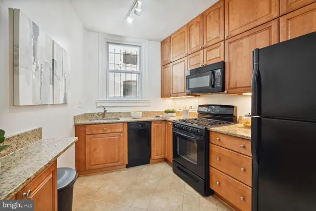 a kitchen with stainless steel appliances granite countertop a stove top oven a sink dishwasher and a refrigerator with wooden cabinets