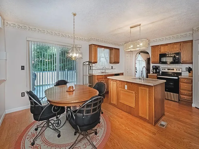 a kitchen with stainless steel appliances granite countertop a stove a sink a refrigerator a dining table and chairs