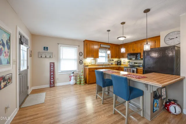 a kitchen with stainless steel appliances granite countertop a refrigerator a sink dishwasher a dining table and chairs with wooden floor