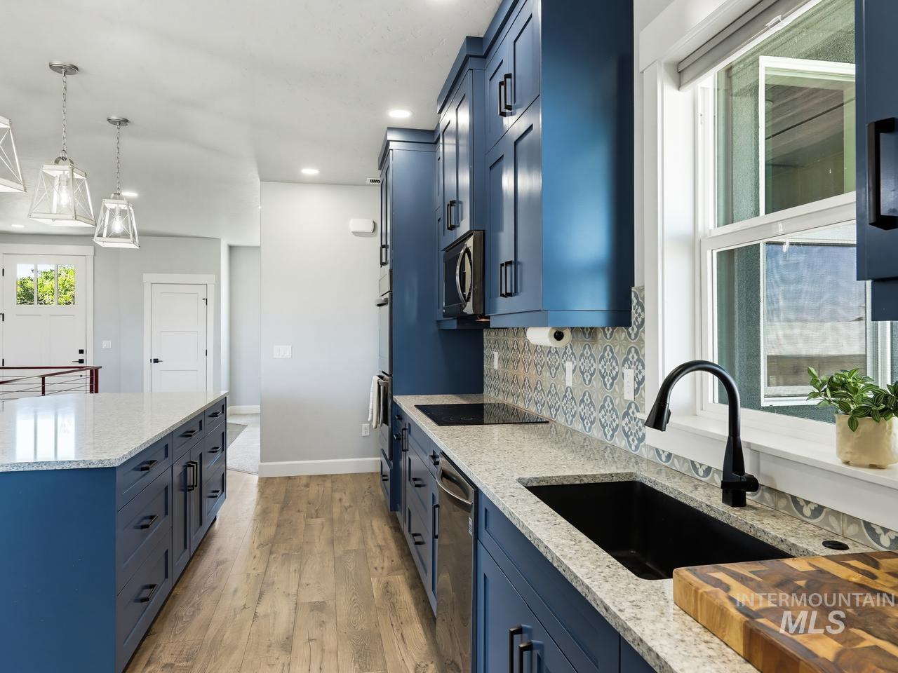 4950 West Columbia Road Nampa, ID 83687 - Photo 16 of 50 Kitchen featuring blue cabinetry, light-colored countertops, wood-finish flooring, a patterned tile backsplash, and stainless steel appliances