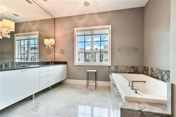 a bathroom with a bathtub a double vanity sink a window and a mirror