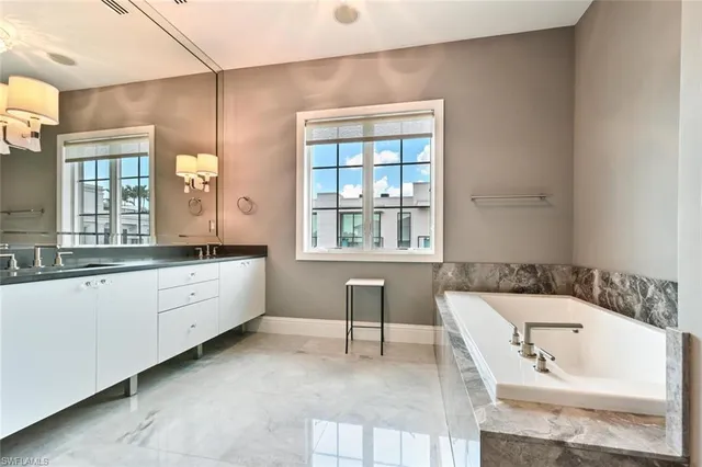 a bathroom with a bathtub a double vanity sink a window and a mirror