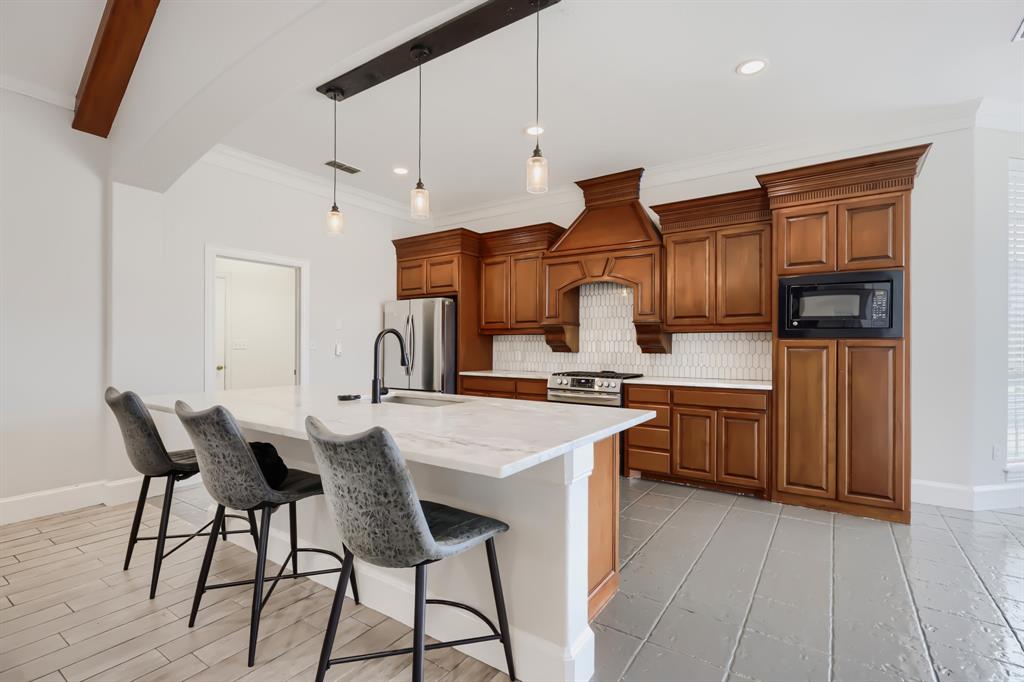 603 Ash Street Pilot Point, TX 76258 - Photo 15 of 28 Spacious kitchen featuring a large central island with a stone countertop, warm wood cabinetry, built-in microwave, stainless steel range, and tile flooring