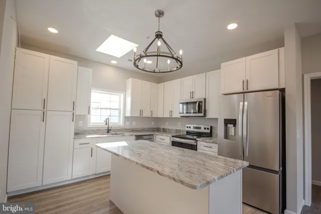 a kitchen with stainless steel appliances granite countertop a refrigerator a sink dishwasher a stove and white cabinets with wooden floor