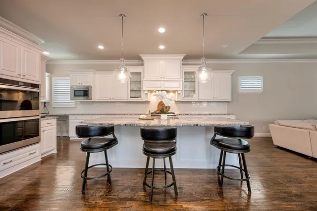 a kitchen with stainless steel appliances granite countertop a stove a sink a refrigerator and chairs with wooden floor