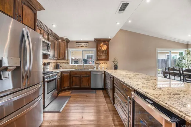 a kitchen with stainless steel appliances granite countertop a refrigerator a sink dishwasher a stove with wooden cabinets and floor