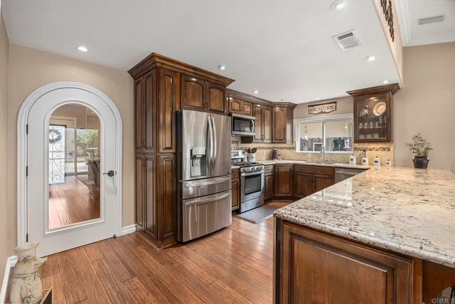 a kitchen with stainless steel appliances granite countertop a refrigerator a stove and a sink with wooden floor
