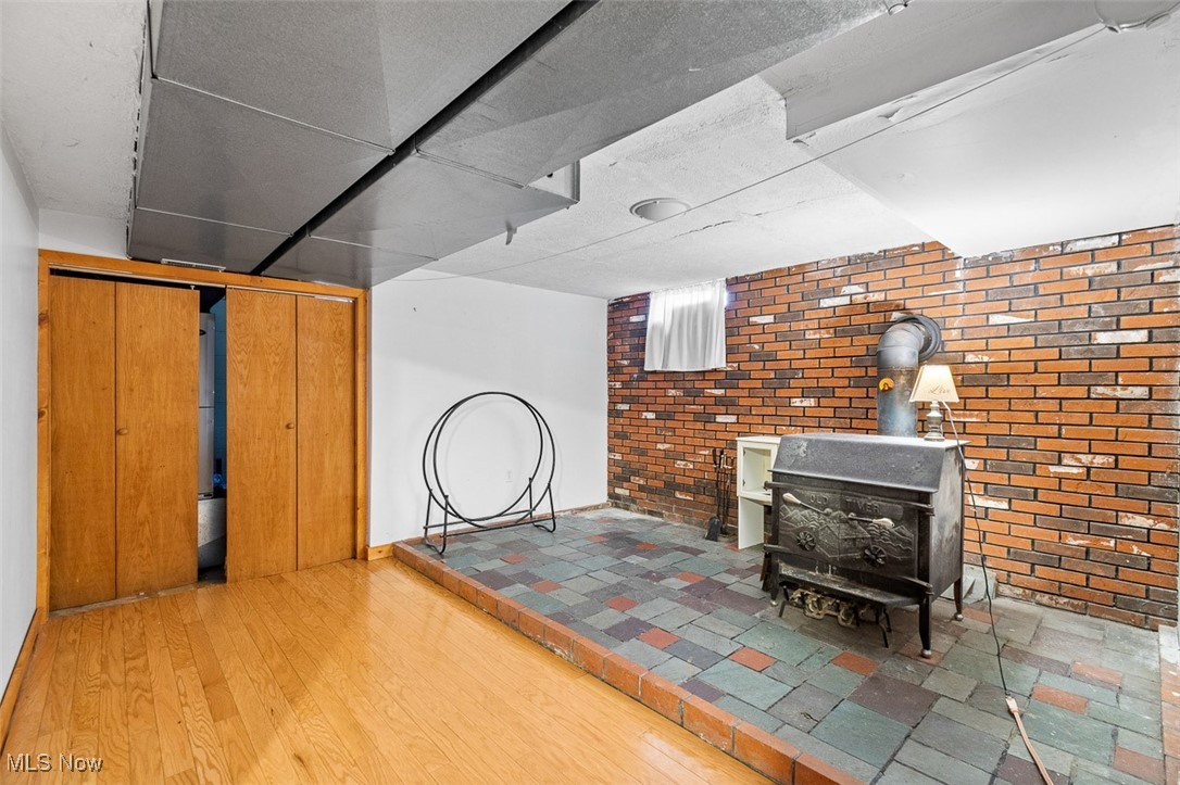 5208 Canaan Center Road Wooster, OH 44691 - Photo 24 of 33 Finished basement with a wood stove, wood finished floors, and brick wall