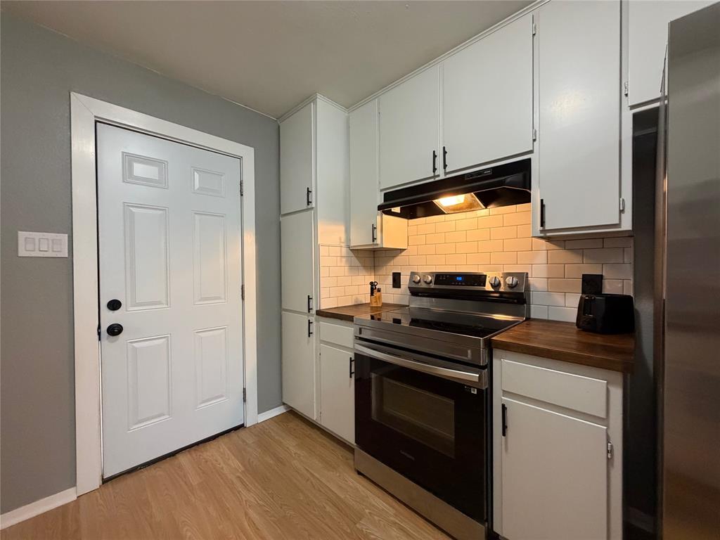508 Batterson Street Cleburne, TX 76031 - Photo 10 of 28 Kitchen featuring wood-finish flooring, white cabinetry with black hardware, subway tile backsplash, stainless steel range, and wood-finish countertops