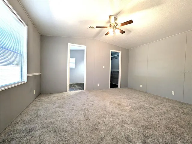 an empty room with chandelier fan and windows