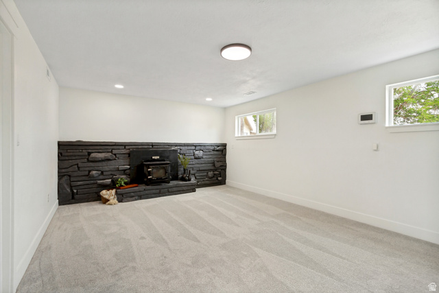 62 South Clark Lane Elk Ridge, UT 84651 - Photo 19 of 30 Spacious flex/family room featuring a dark stacked stone accent wall with a wood-burning stove, light gray carpeting, and white baseboards. This room has the dry bar.