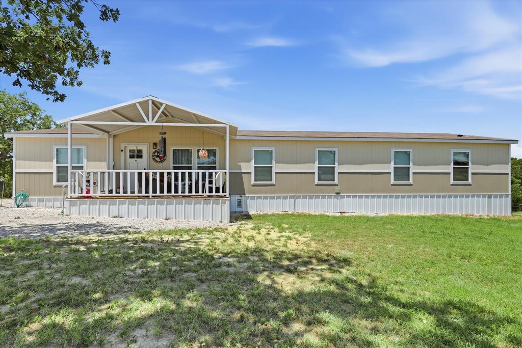 193 Firefly Drive Springtown, TX 76082 - Photo 2 of 32 Single-story residence featuring a covered front porch with white railing, light-colored siding, multiple windows, and a gravel driveway