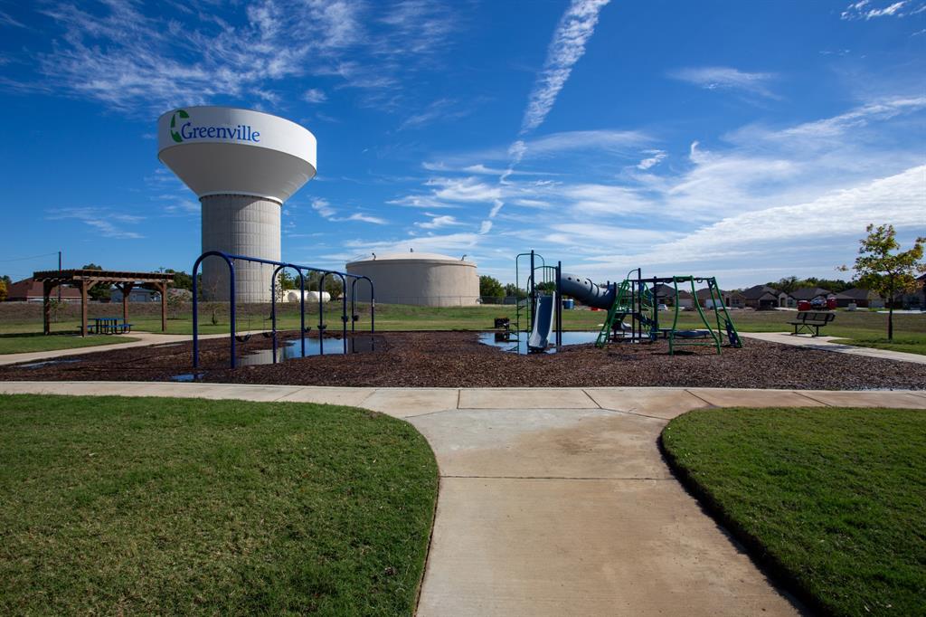 804 Ransom Way Greenville, TX 75402 - Photo 17 of 22 Community playground featuring a slide, swings, and climbing structures on a wood chip base, bordered by concrete pathways and manicured lawns