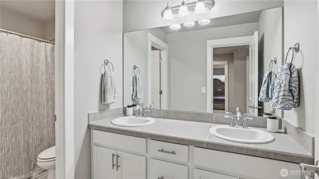 a bathroom with double vanity sinks a toilet a mirror and shower curtain