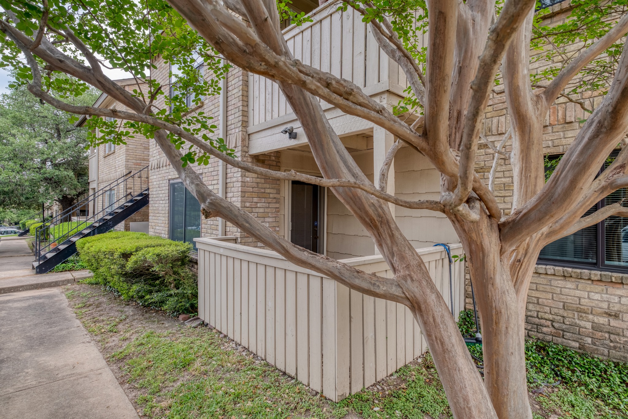 8210 Bent Tree Road, Unit 153 Austin, TX 78759 - Photo 4 of 20 Brick exterior featuring a private patio with a slatted privacy wall, mature tree, manicured shrubs, and a concrete walkway