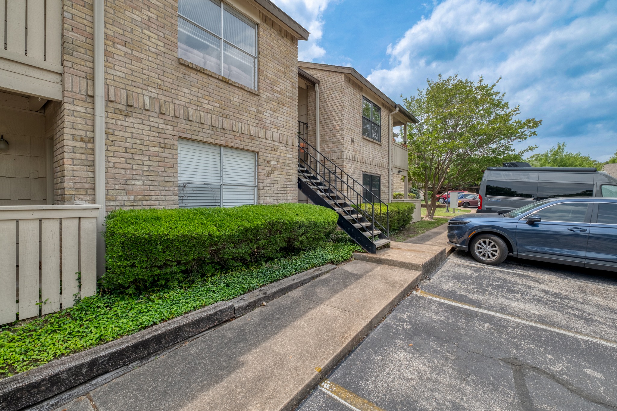 8210 Bent Tree Road, Unit 153 Austin, TX 78759 - Photo 5 of 20 Multi-story brick exterior featuring a black metal staircase, mature landscaping, and an asphalt parking area