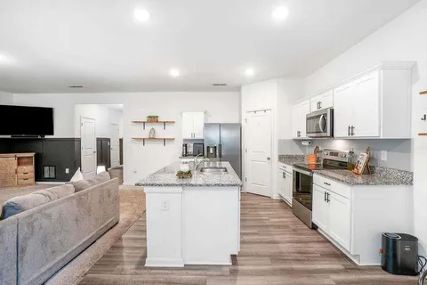 a large kitchen with stainless steel appliances kitchen island granite countertop a stove a sink a refrigerator and white cabinets with wooden floor