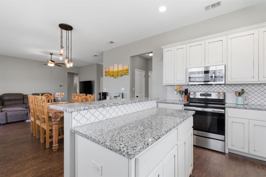 711 Hadley Lane Valley View, TX 76272 - Photo 10 of 40 Kitchen with stainless steel appliances, white cabinets, ceiling fan, decorative light fixtures, and light stone countertops