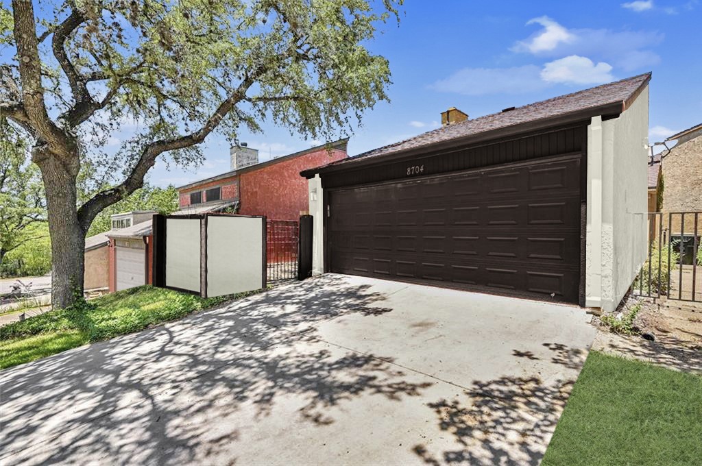 8704 Merion Circle Austin, TX 78754 - Photo 15 of 16 Attached garage with a dark brown sectional door, concrete driveway, and a sloped roofline
