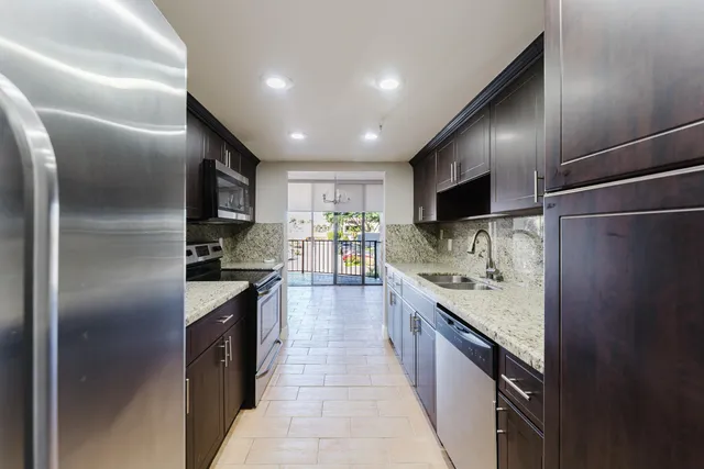 a large kitchen with stainless steel appliances kitchen island granite countertop a refrigerator and a sink