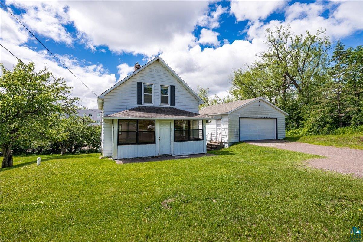 424 East Upham Road Duluth, MN 55811 - Photo 24 of 38 White-sided residence featuring a covered front porch with dark-framed windows, a detached single-car garage, mature trees, and a gravel driveway