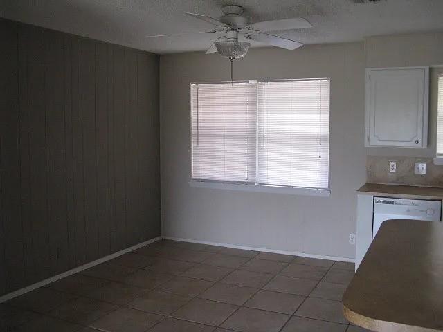 4004 Vicky Street Big Spring, TX 79720 - Photo 6 of 13 Dining area featuring a ceiling fan with light fixture, large window with blinds, tile flooring, and a paneled accent wall