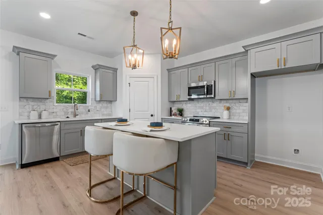 a open kitchen with stainless steel appliances granite countertop a sink dishwasher a stove a refrigerator and white cabinets with wooden floor
