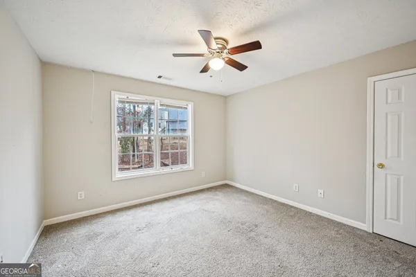 an empty room with a chandelier fan and a kitchen area