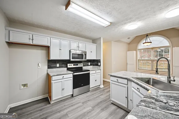 a kitchen with stainless steel appliances granite countertop a stove a sink dishwasher a refrigerator white cabinets and wooden floor