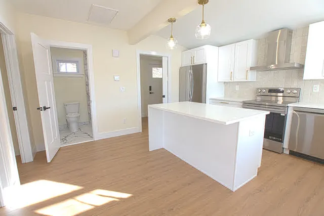 a kitchen with stainless steel appliances granite countertop a refrigerator a sink dishwasher a stove and white countertops with wooden floor