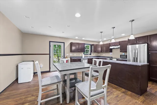 a dining room with stainless steel appliances kitchen island granite countertop a table chairs and a refrigerator