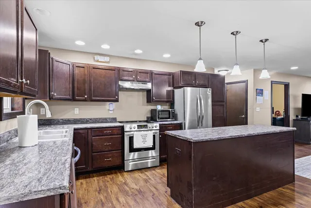 a kitchen with stainless steel appliances granite countertop a stove a sink a refrigerator and a oven with wooden floor